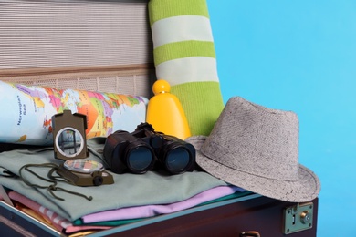 Photo of Open vintage suitcase with clothes packed for summer vacation on light blue background, closeup
