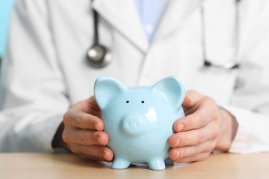 Photo of Doctor with piggy bank at wooden table, closeup