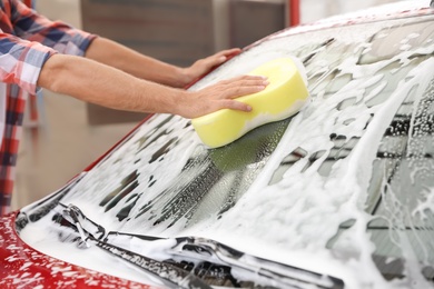 Man washing red auto with sponge at car wash, closeup