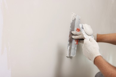 Photo of Worker plastering wall with putty knife indoors, closeup. Space for text