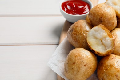 Photo of Tasty whole baked potatoes and sauce on white wooden table, closeup. Space for text