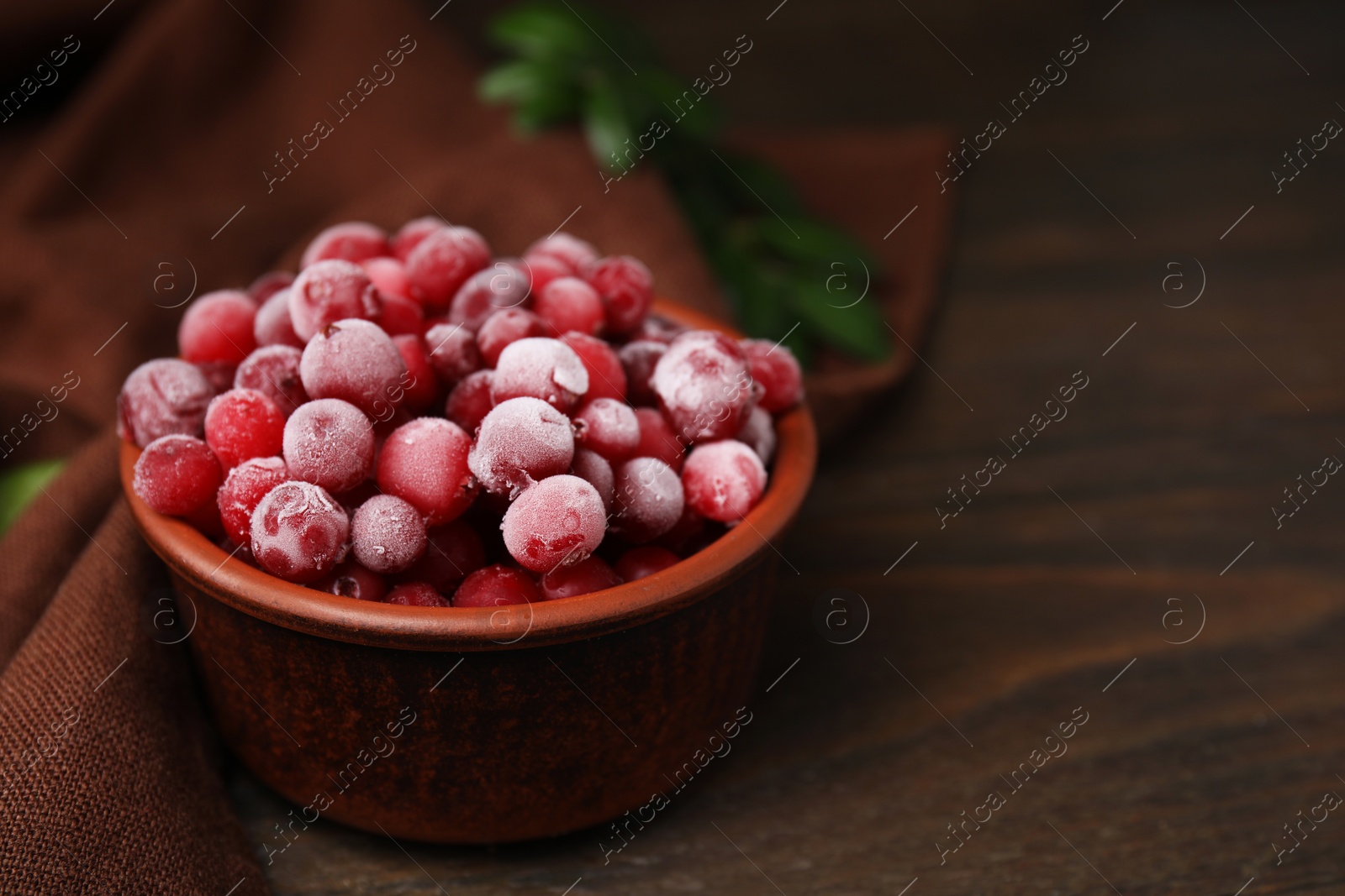 Photo of Frozen red cranberries in bowl on wooden table, closeup. Space for text