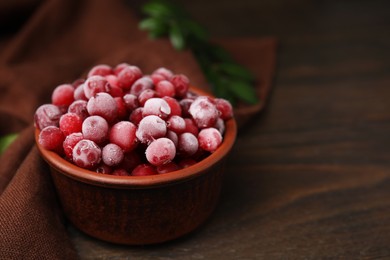 Photo of Frozen red cranberries in bowl on wooden table, closeup. Space for text