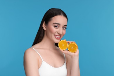 Beautiful young woman with pieces of orange on light blue background