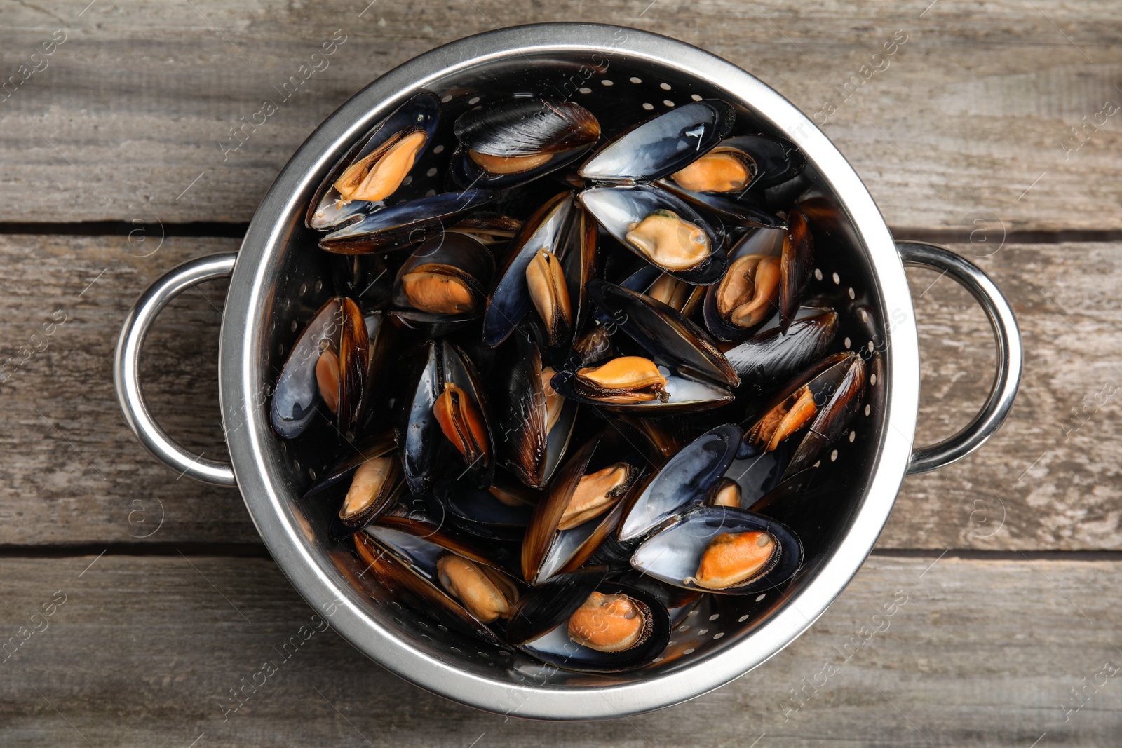 Photo of Colander with delicious cooked mussels on wooden table, top view