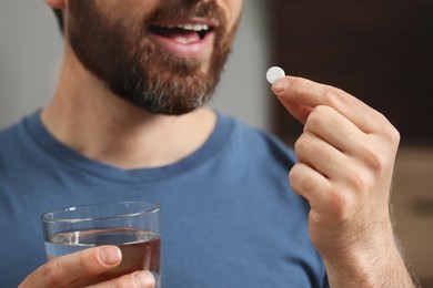 Photo of Man with glass of water taking pill on blurred background, closeup