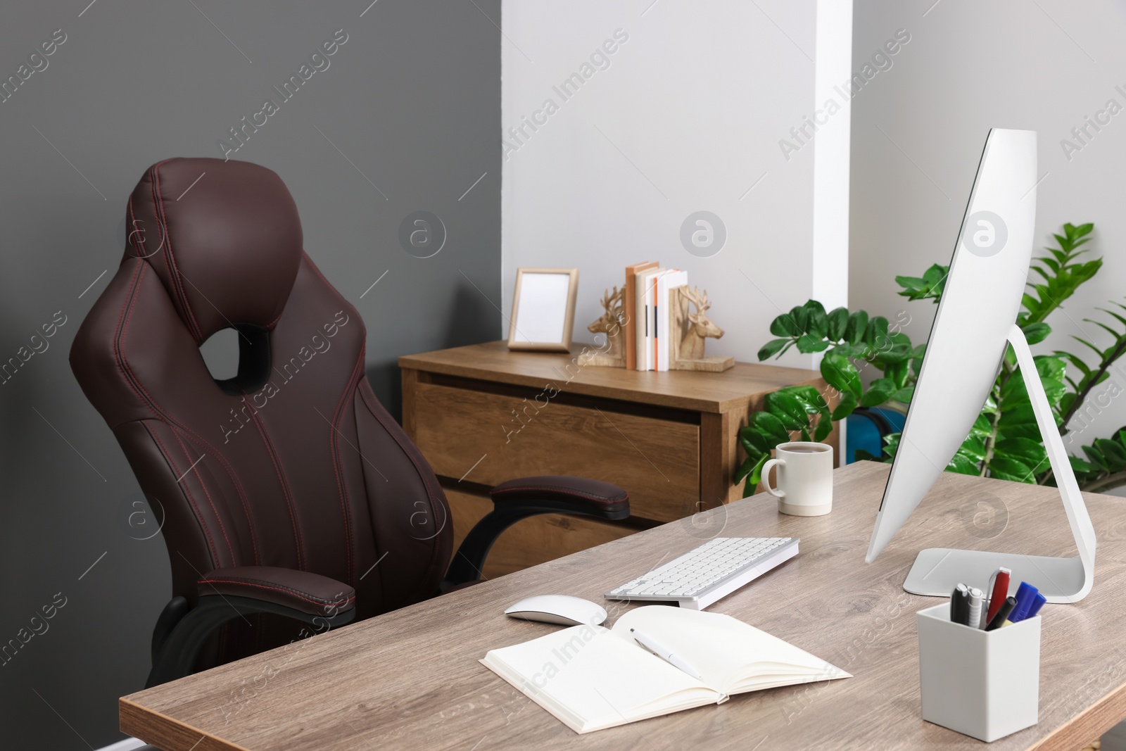 Photo of Computer, notebook and stationery on table near chair in office. Boss workplace