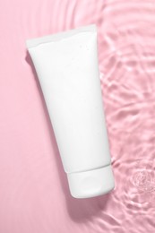 Tube of facial cleanser in water against pink background, top view