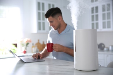 Man using laptop in kitchen with modern air humidifier