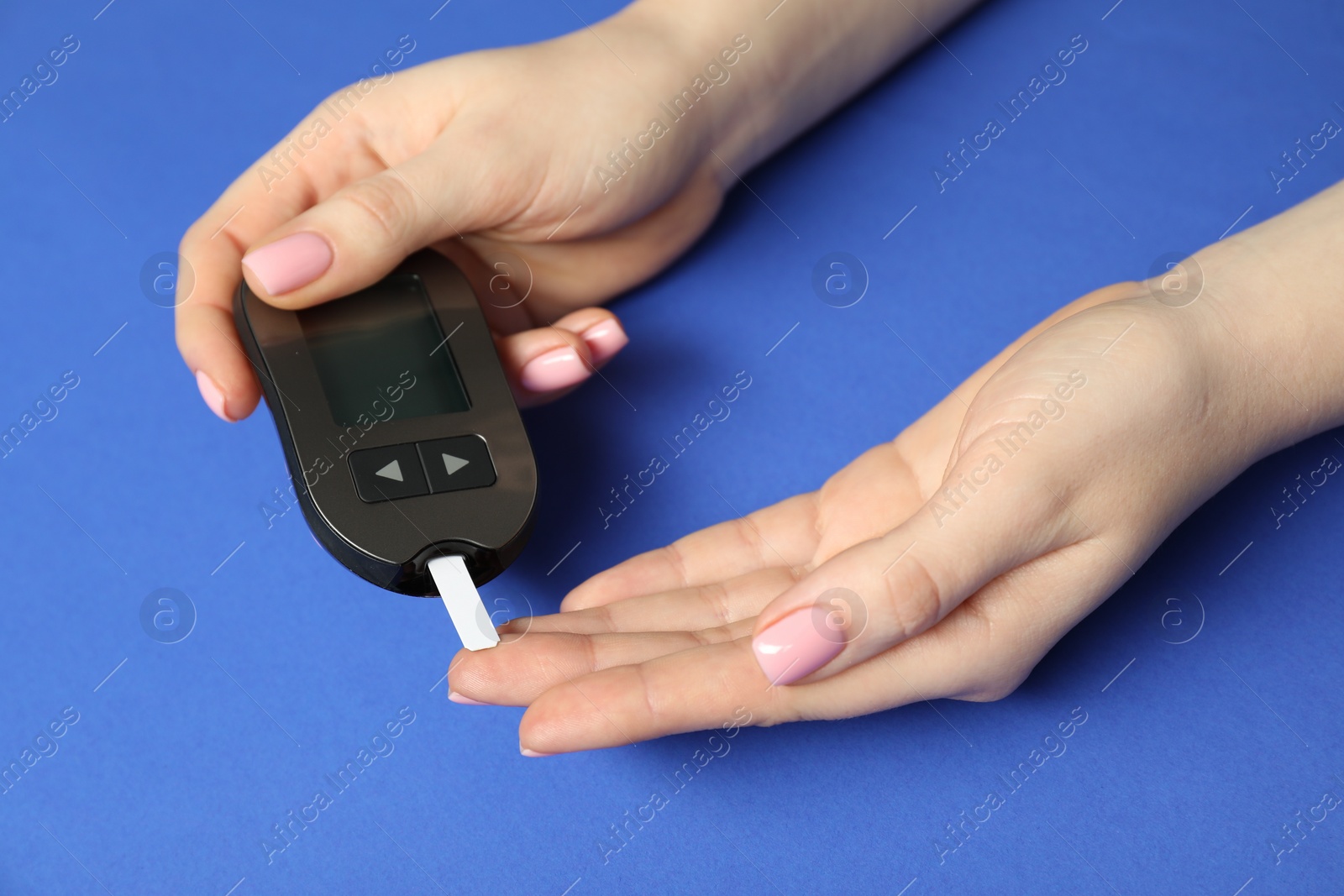 Photo of Diabetes. Woman checking blood sugar level with glucometer on blue background, closeup