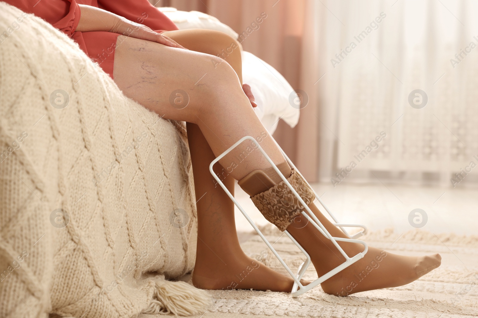 Photo of Woman putting on compression tights with stocking donner in bedroom, closeup. Prevention of varicose veins