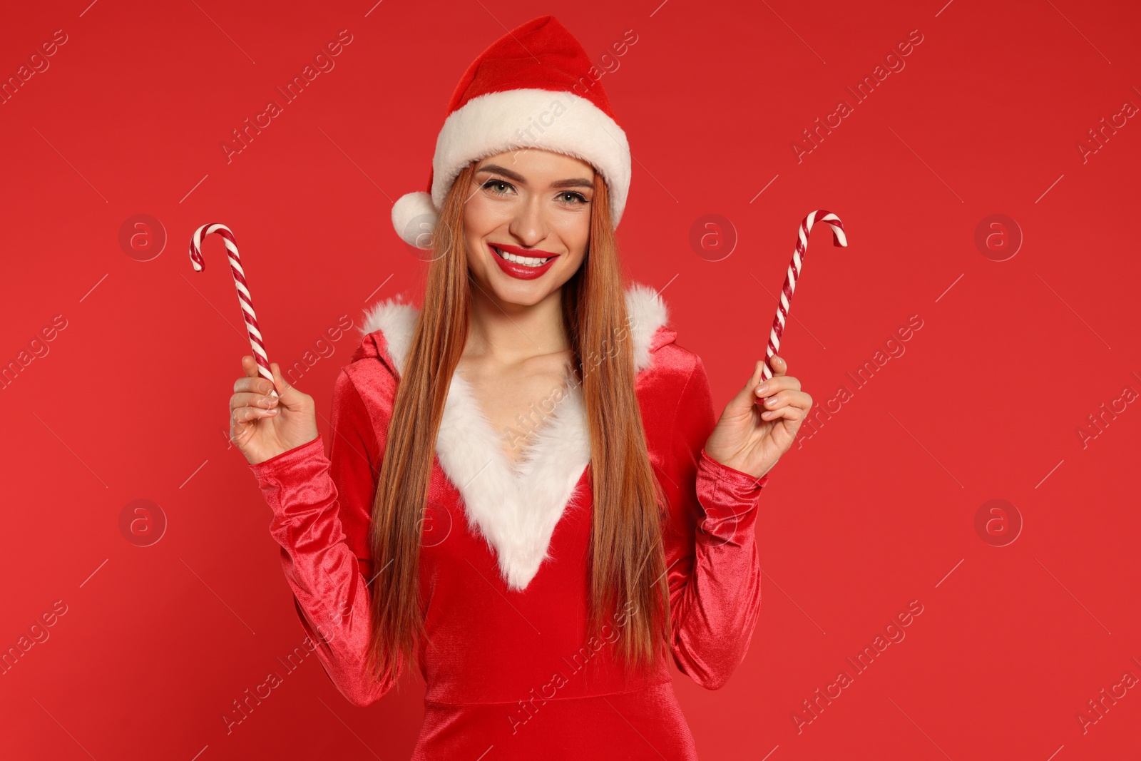 Photo of Young woman in Santa hat with candy canes on red background. Christmas celebration