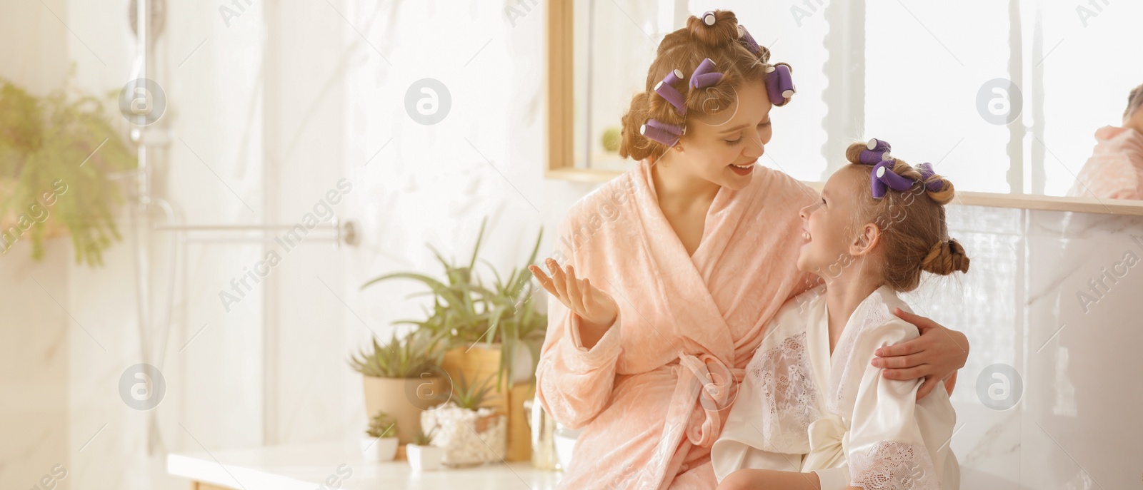 Image of Happy mother and daughter with curlers in bathroom. Banner design