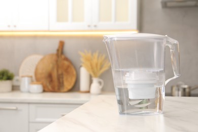 Photo of Water filter jug on white marble table in kitchen, space for text