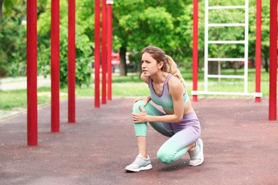 Young woman suffering from knee pain on sports ground