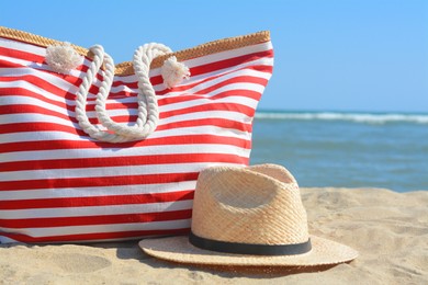 Photo of Stylish striped bag with straw hat on sandy beach near sea