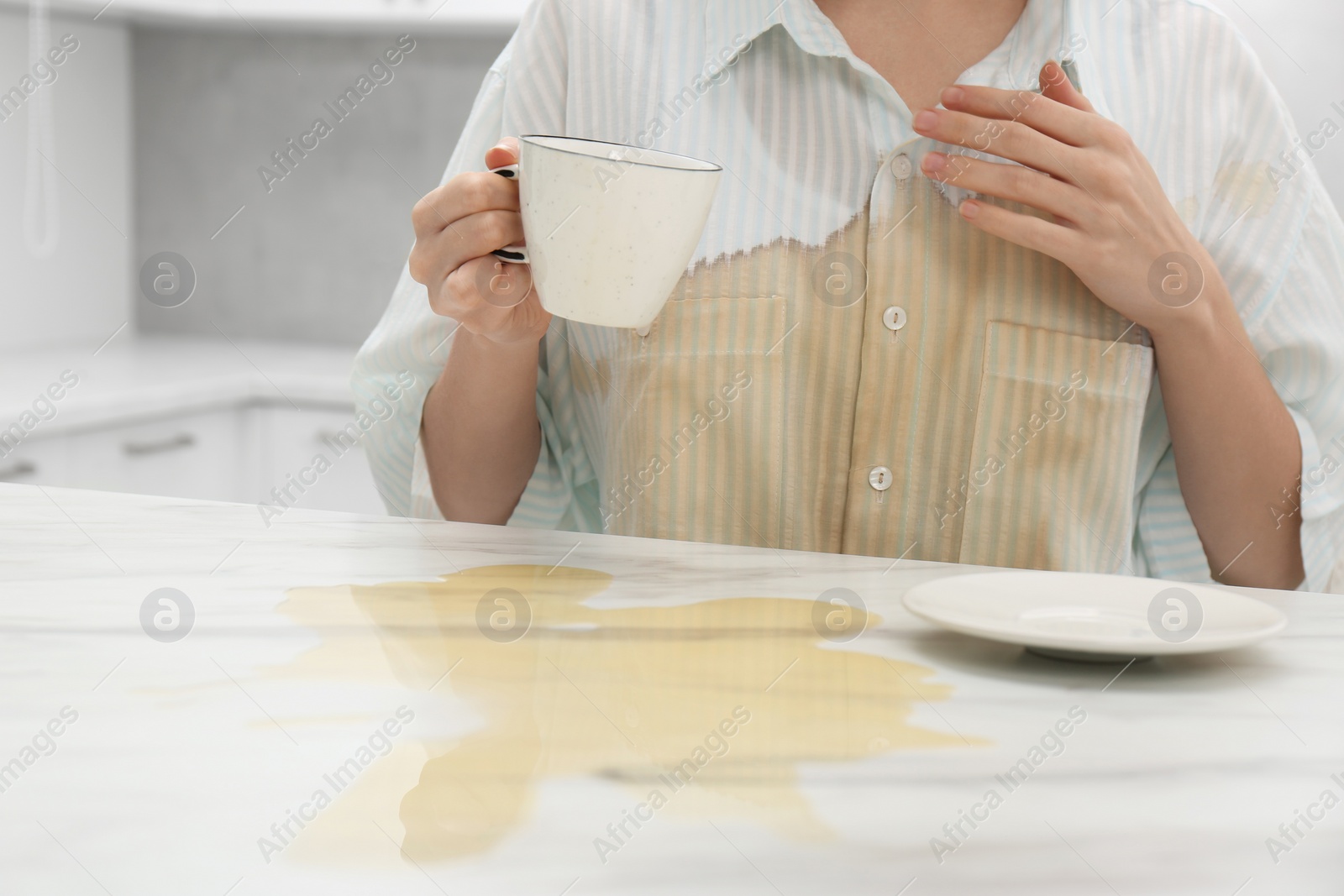 Photo of Woman with spilled coffee over her shirt at marble table in kitchen, closeup