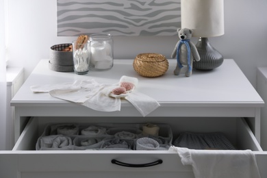 Modern open chest of drawers with baby clothes and accessories in room