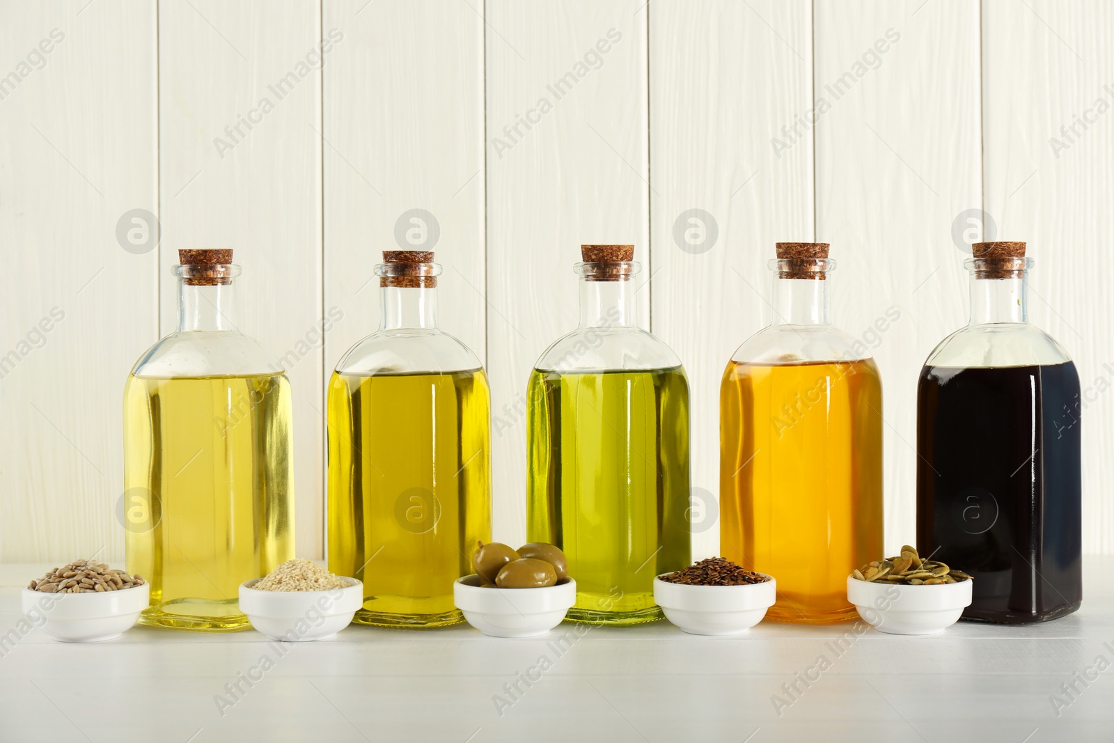 Photo of Vegetable fats. Different cooking oils in glass bottles and ingredients on white wooden table