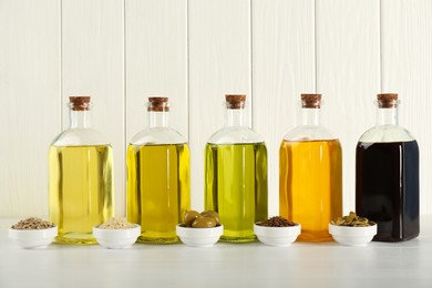 Photo of Vegetable fats. Different cooking oils in glass bottles and ingredients on white wooden table