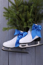 Pair of ice skates with fir branches hanging on grey wooden wall