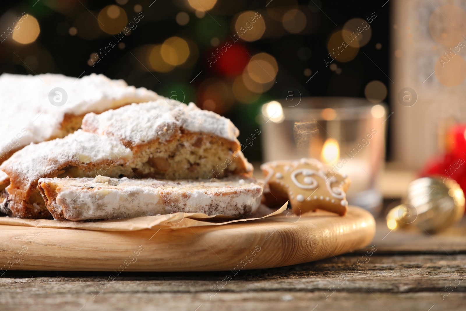Photo of Traditional Christmas Stollen with icing sugar on wooden table against blurred festive lights