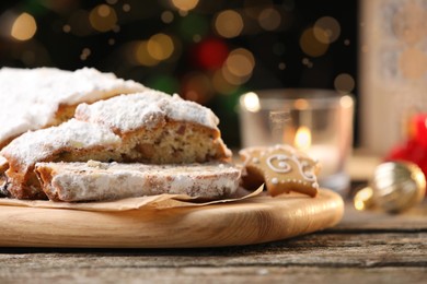 Traditional Christmas Stollen with icing sugar on wooden table against blurred festive lights