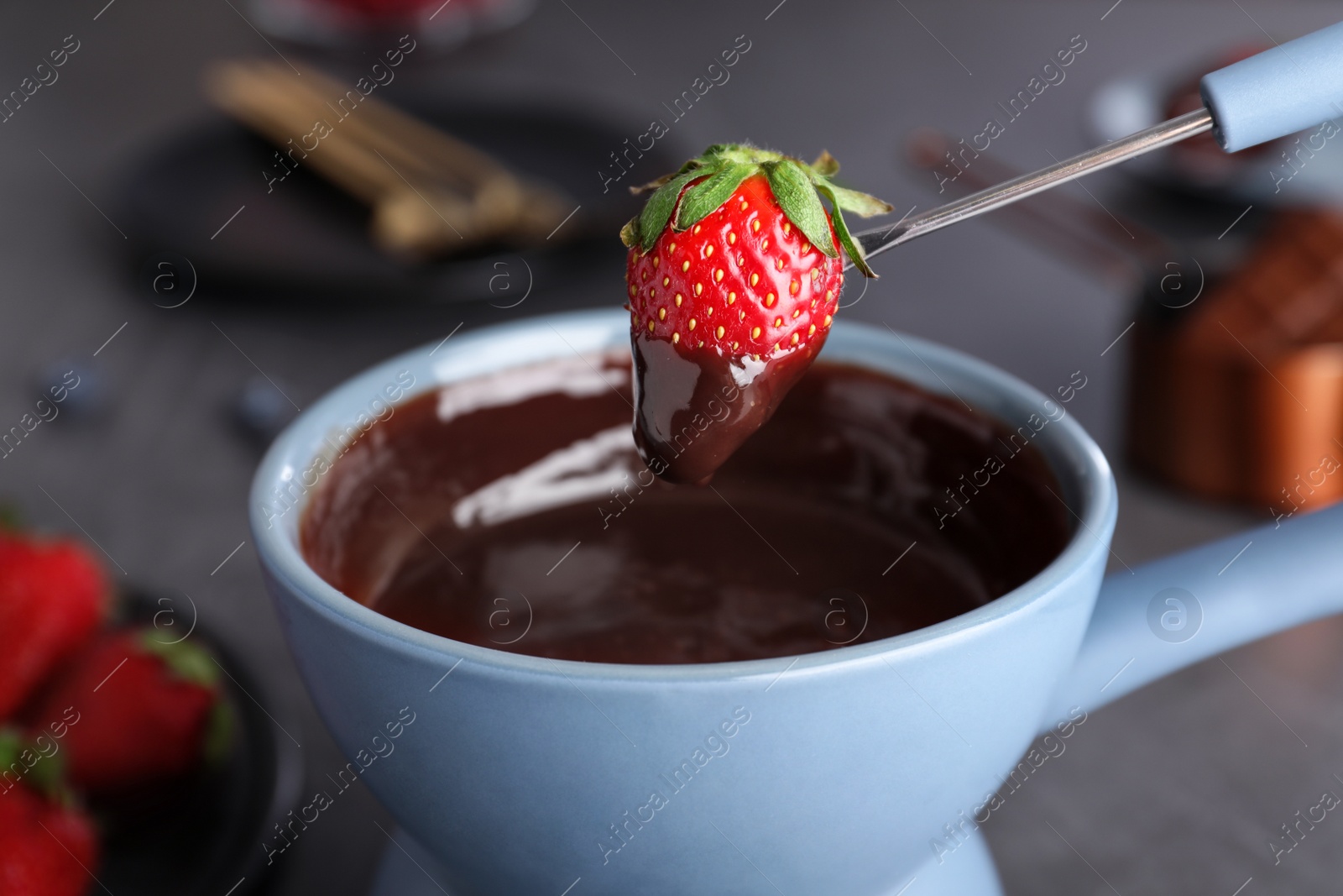 Photo of Dipping strawberry into pot with chocolate fondue on table, closeup