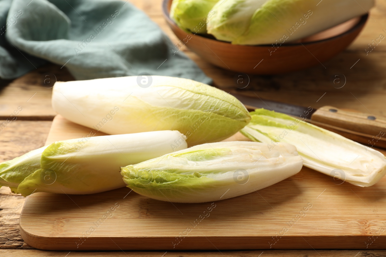 Photo of Fresh raw Belgian endives (chicory), board and knife on wooden table, closeup