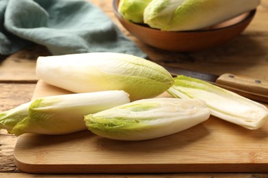 Photo of Fresh raw Belgian endives (chicory), board and knife on wooden table, closeup