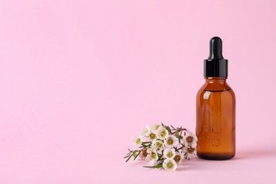 Photo of Bottle with cosmetic oil and flowers on pink background, space for text