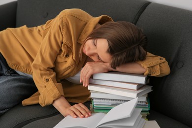 Photo of Young tired woman sleeping near books on couch