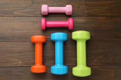 Different dumbbells on wooden table, flat lay