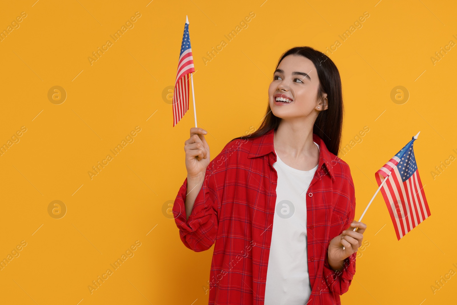 Photo of 4th of July - Independence Day of USA. Happy girl with American flags on yellow background, space for text