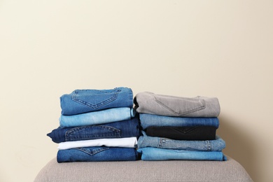 Stack of different jeans on ottoman against light background