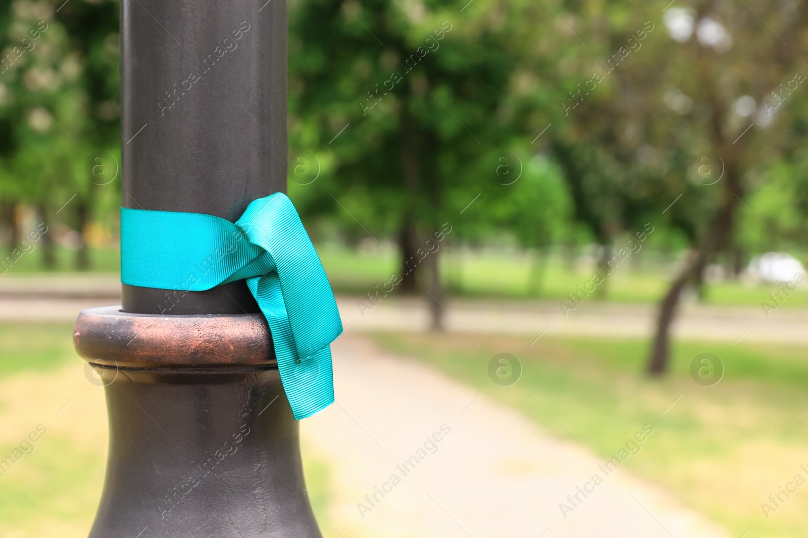 Photo of Teal awareness ribbon tied on lamppost in park, space for text