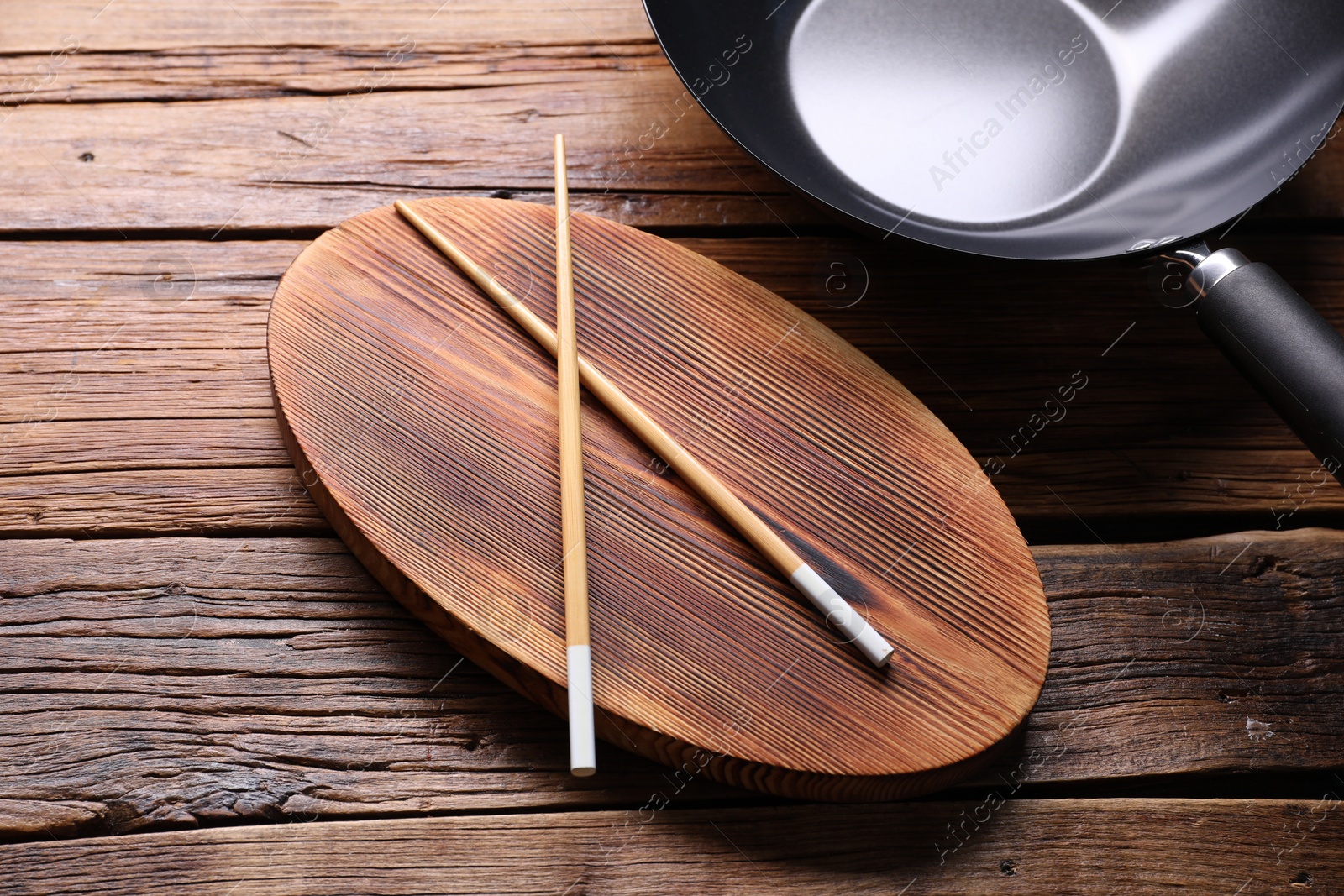 Photo of Serving board with chopsticks and iron wok on wooden table, closeup