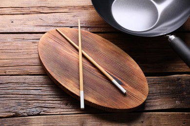 Serving board with chopsticks and iron wok on wooden table, closeup