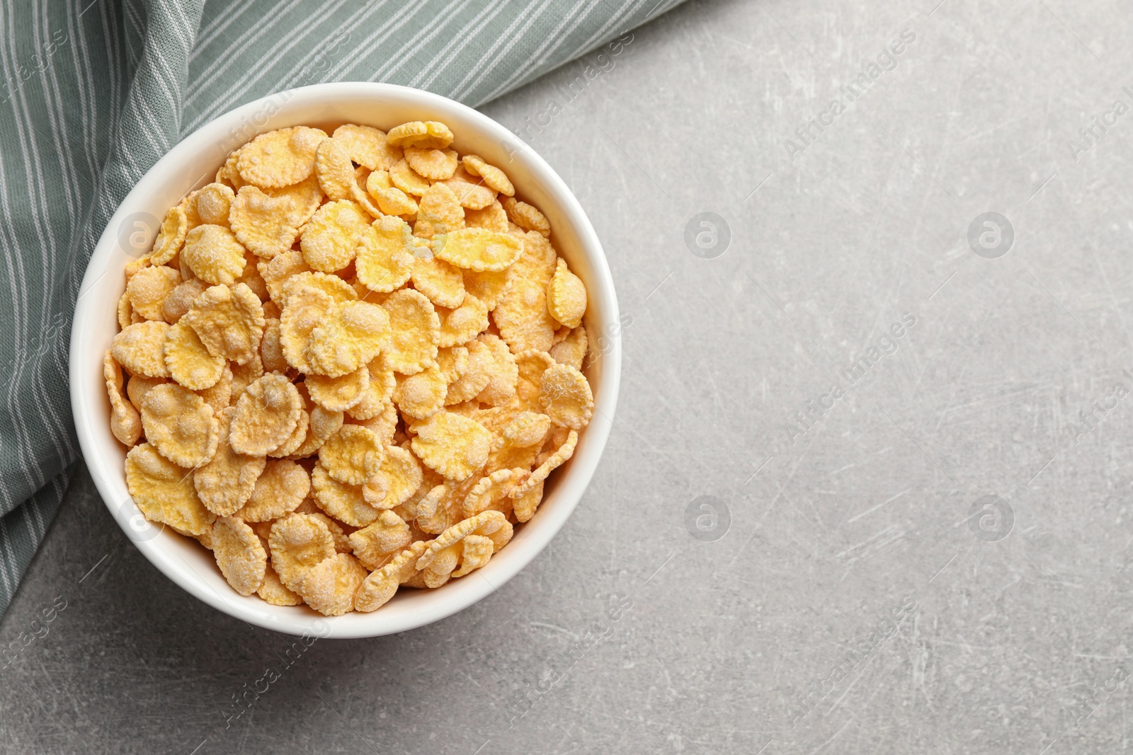 Photo of Bowl of tasty corn flakes on light grey background, top view. Space for text