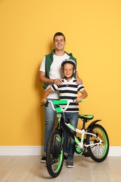 Photo of Portrait of father and his son with bicycle near color wall