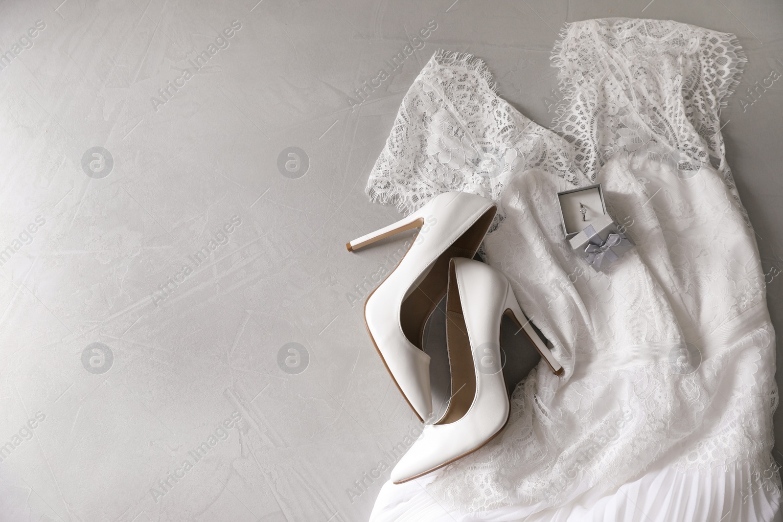 Photo of Wedding dress, white high heel shoes and ring on grey background, flat lay. Space for text