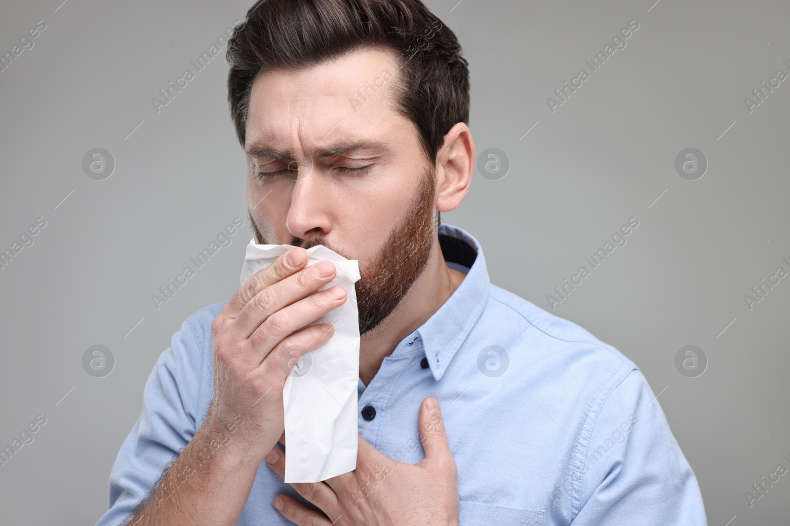 Photo of Sick man with tissue coughing on light grey background