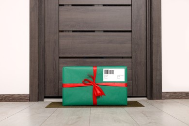 Christmas gift box on floor near door. Sending present by mail