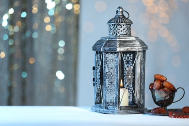 Photo of Arabic lantern, misbaha and dates on table against blurred lights, space for text