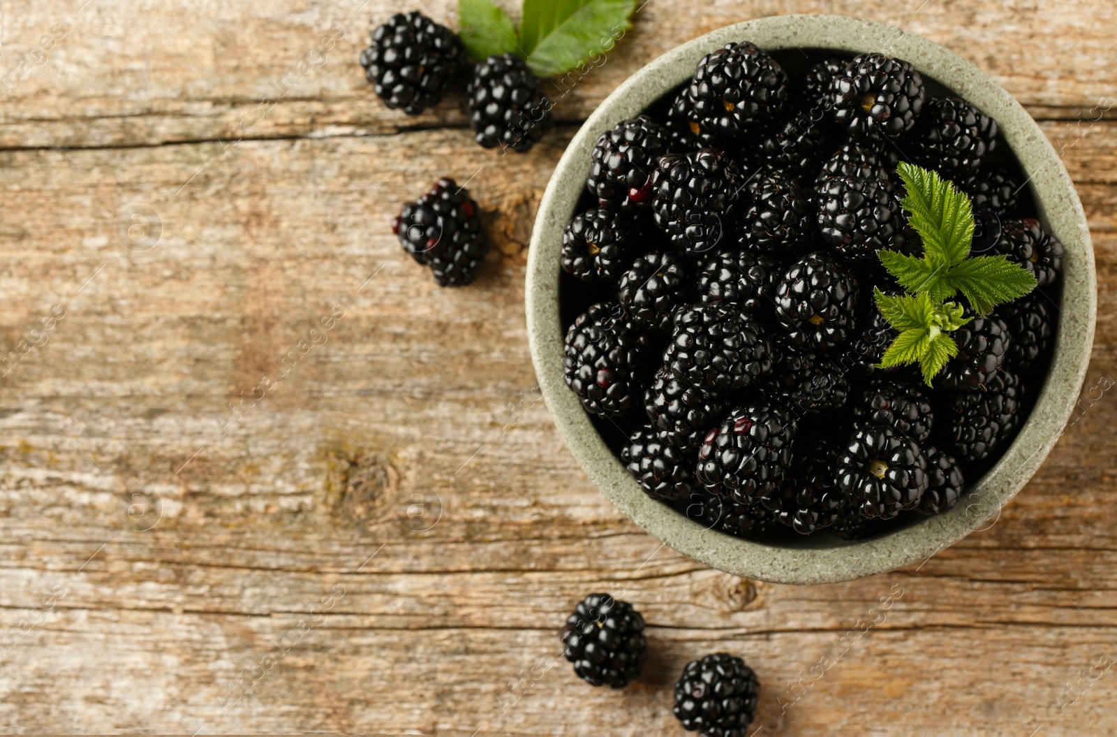 Photo of Bowl and fresh ripe blackberries on wooden table, flat lay. Space for text
