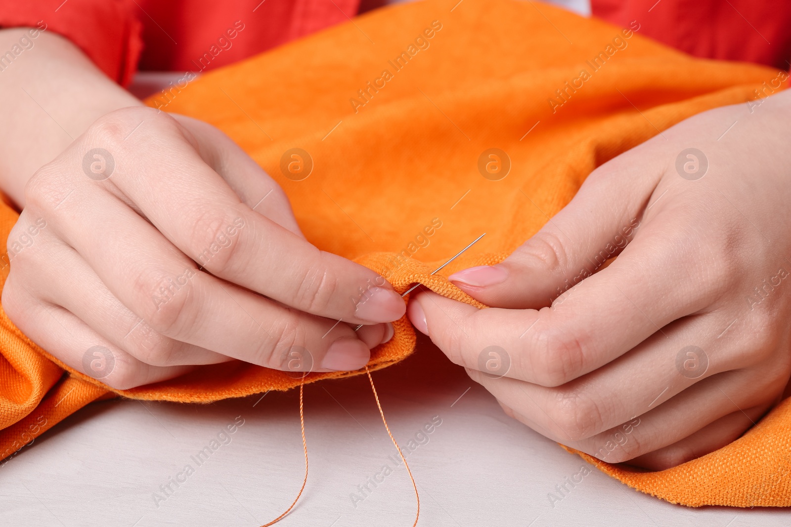 Photo of Woman sewing cloth with needle at light wooden table, closeup