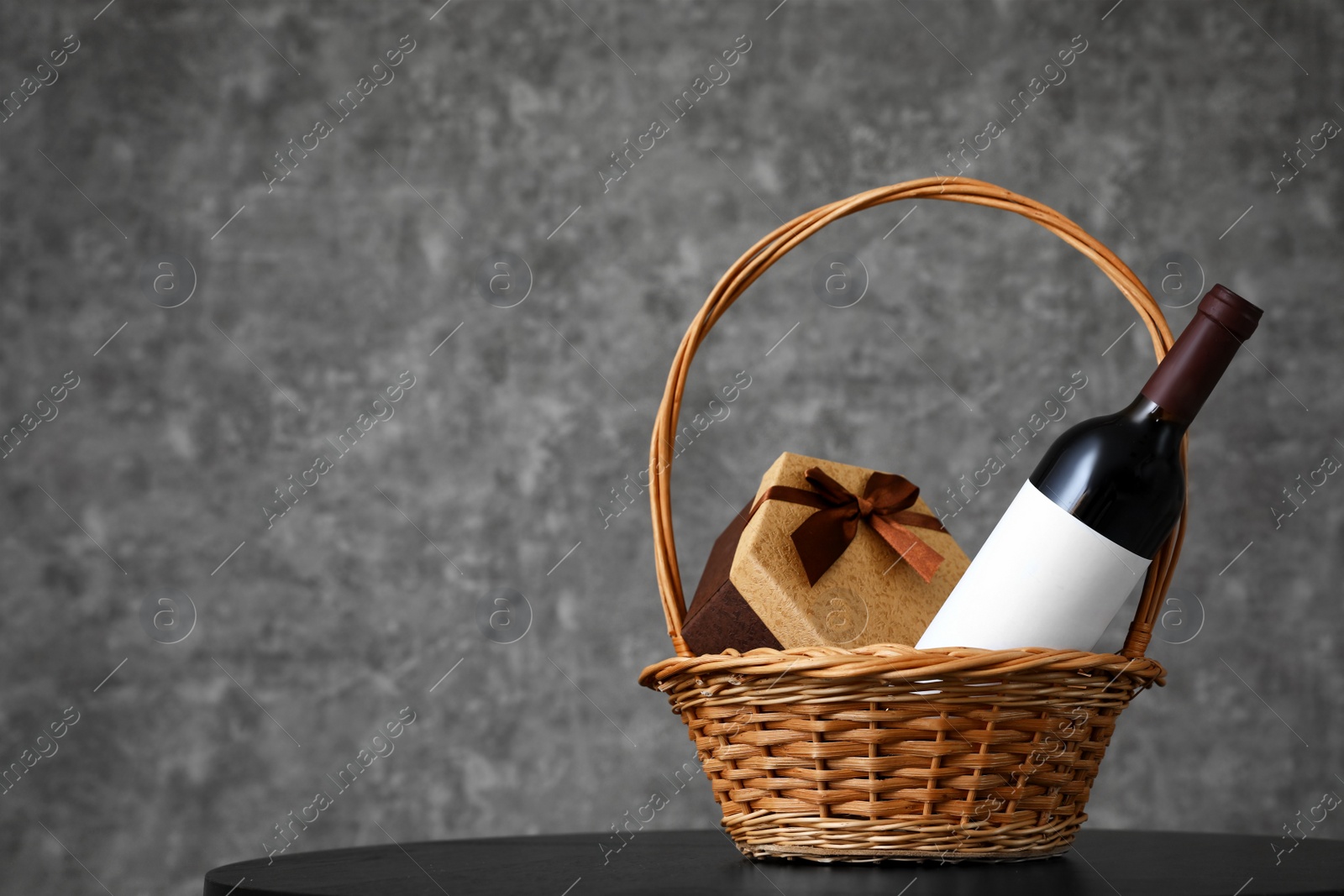 Photo of Wicker basket with bottle of wine and gift box on table. Space for design