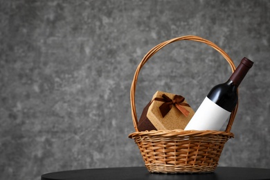 Wicker basket with bottle of wine and gift box on table. Space for design