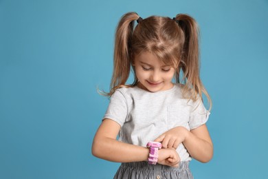 Little girl with smart watch on light blue background, space for text