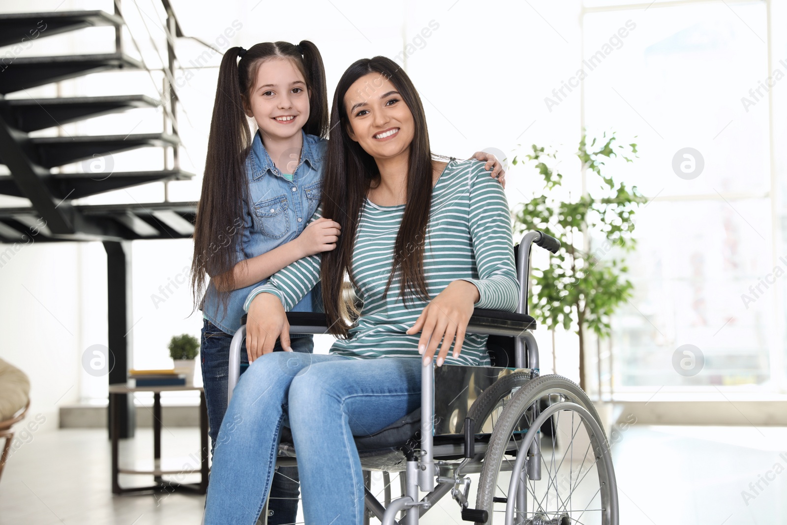 Photo of Young woman in wheelchair with her daughter indoors